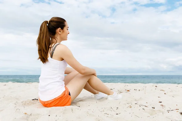 Mladá žena v sportovní oblečení sedí na pláži — Stock fotografie
