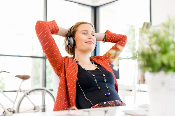 Ung kvinna i office med hörlurar — Stockfoto