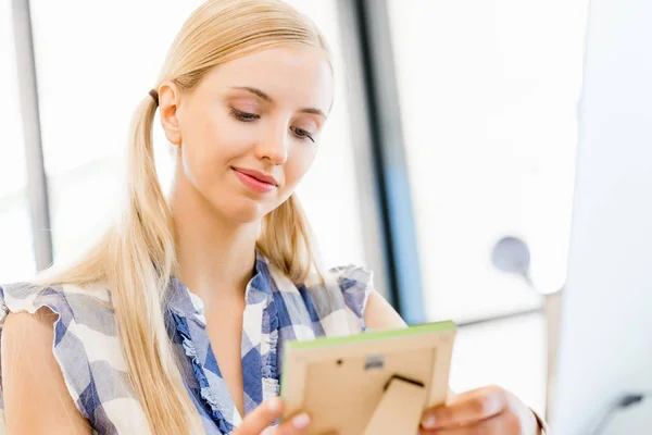 Young woman in office holdinga photo frame — Stock Photo, Image