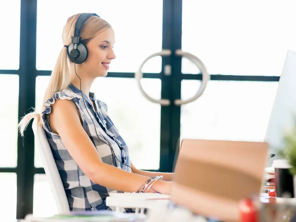 Junge Frau arbeitet im Büro mit Kopfhörern — Stockfoto