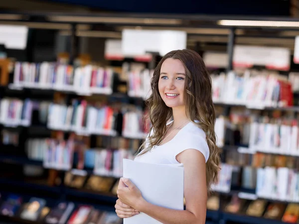 Feliz estudiante sosteniendo libros en la biblioteca —  Fotos de Stock