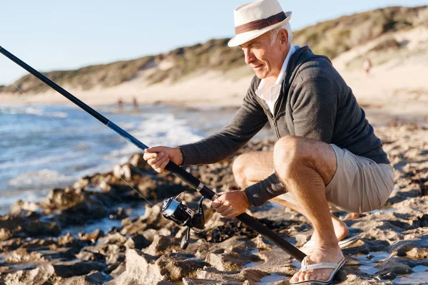 Uomo anziano pesca sul lato mare — Foto Stock