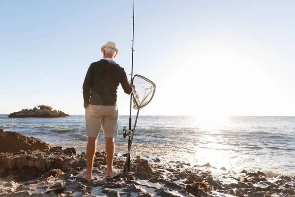 Uomo anziano pesca sul lato mare — Foto Stock