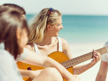 Güzel genç bir kadın sahilde gitar çalıyor.