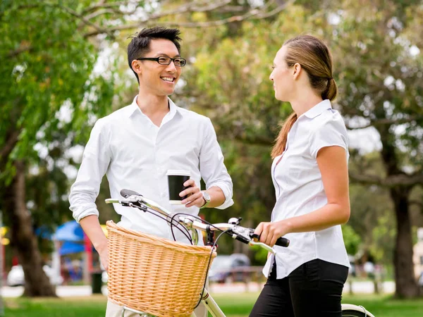 Retrato de pareja sonriente de pie en el parque con bicicleta hablando — Foto de Stock