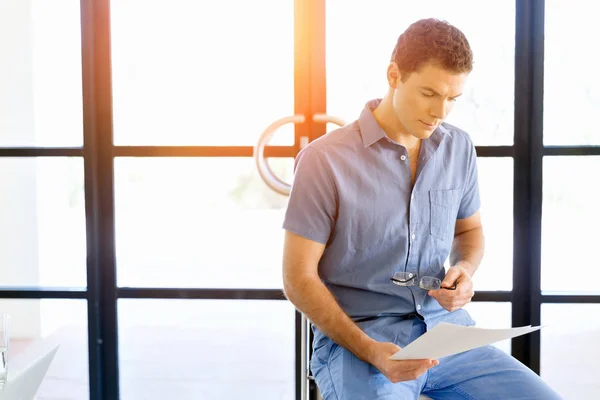 Young business man sitting on a stool in office — Stock Photo, Image