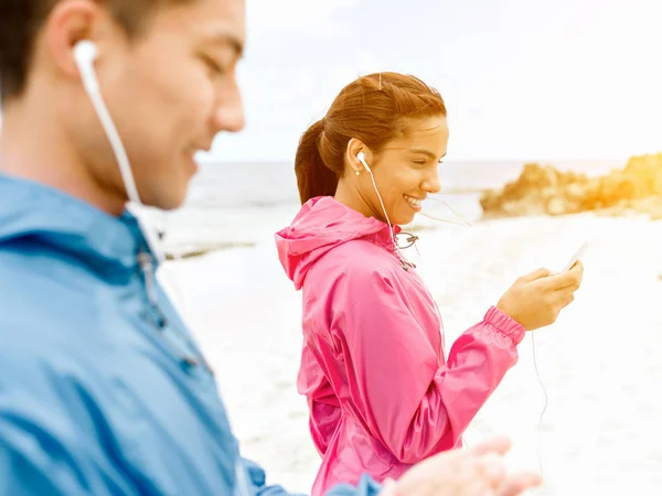 Sportos fiatal pár fülhallgató a tenger partján — Stock Fotó