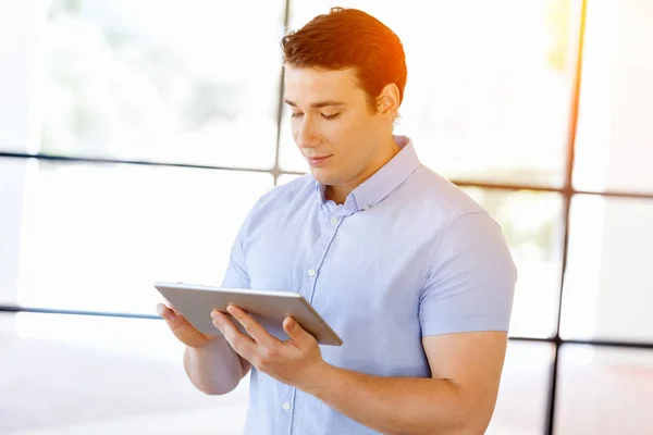 Joven hombre de negocios guapo usando su touchpad de pie en la oficina — Foto de Stock