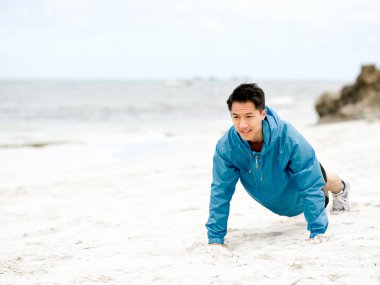 Genç adam sahilde egzersiz yaparak