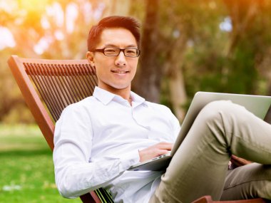 Genç işadamı açık havada otururken dizüstü bilgisayar kullanarak