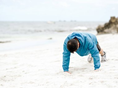 Genç adam sahilde egzersiz yaparak