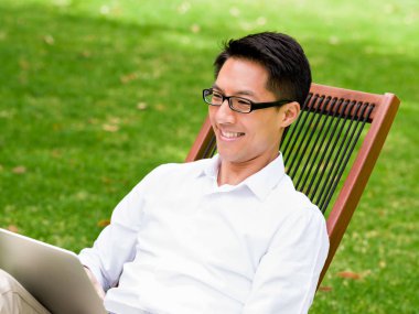 Genç işadamı açık havada otururken dizüstü bilgisayar kullanarak