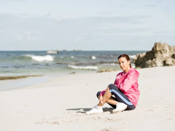 Giovane donna seduta in spiaggia in abbigliamento sportivo — Foto Stock