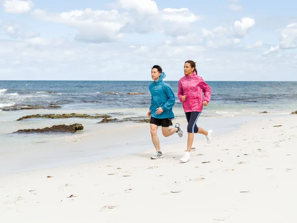 Pareja joven corriendo a lo largo de la orilla del mar — Foto de Stock