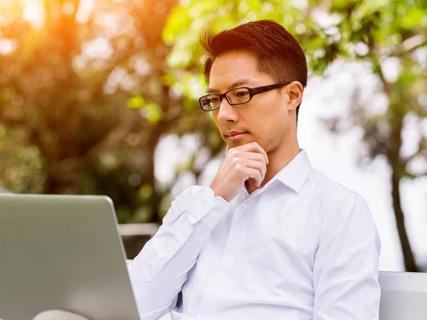 Genç işadamı açık havada otururken dizüstü bilgisayar kullanarak