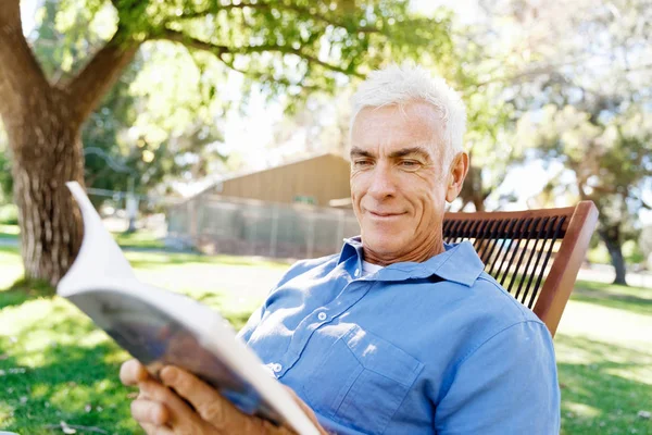 Senior man sittingin park tijdens het lezen van boek — Stockfoto