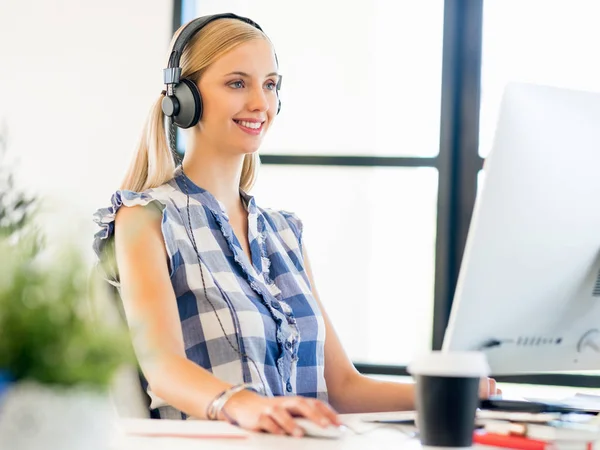 Junge Frau arbeitet im Büro mit Kopfhörern — Stockfoto