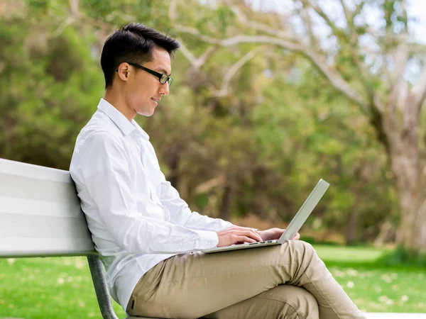 Genç işadamı açık havada otururken dizüstü bilgisayar kullanarak