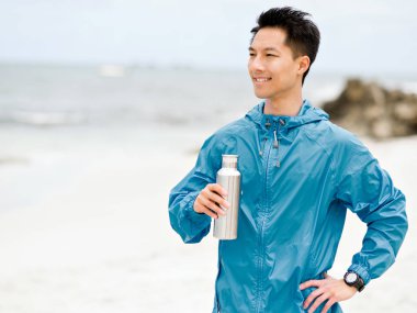 Sporda genç adam içme suyu egzersiz yaptıktan sonra kumsalda elbise