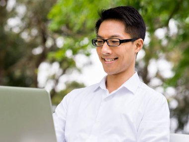 Genç işadamı açık havada otururken dizüstü bilgisayar kullanarak