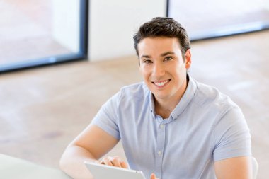 Genç yakışıklı işadamı ofisinde oturup onun touchpad kullanarak