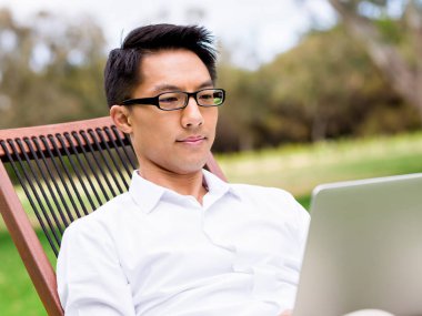 Genç işadamı açık havada otururken dizüstü bilgisayar kullanarak