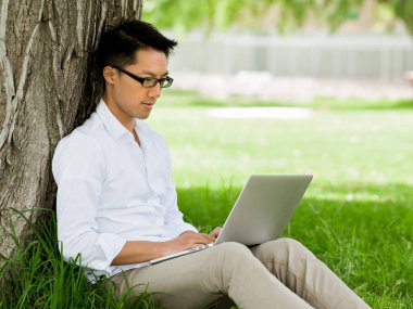 Genç işadamı açık havada otururken dizüstü bilgisayar kullanarak