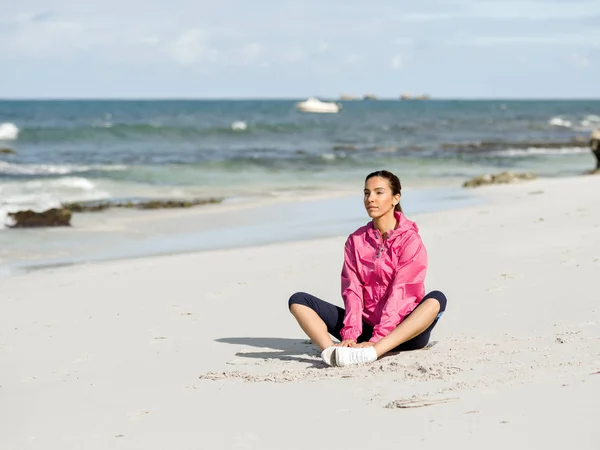 Jonge vrouw zittend op het strand in sportkleding — Stockfoto