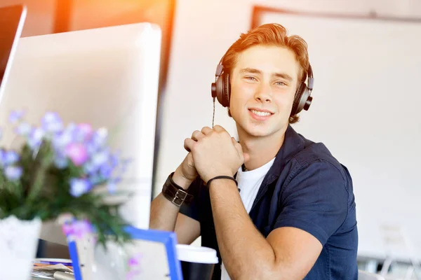 Młody człowiek w biurze ze słuchawkami — Zdjęcie stockowe