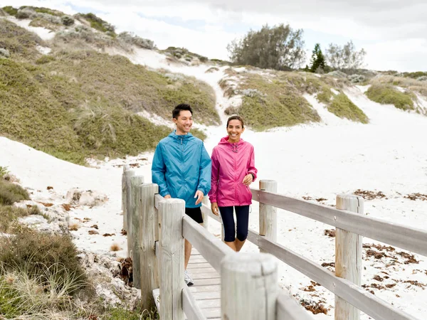 Молодой человек и женщина в спортивной одежде прогуливаются по пляжу — стоковое фото