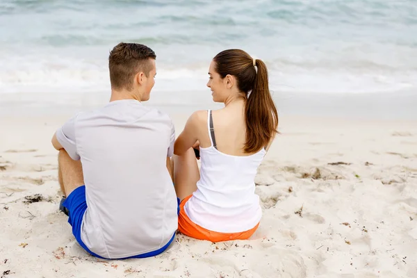 Jeune couple se regardant tout en étant assis sur la plage — Photo