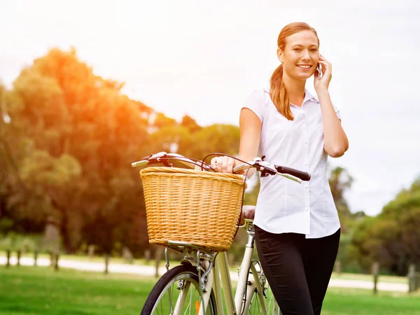 Красивая молодая блондинка с велосипедом в парке разговаривает по телефону — стоковое фото