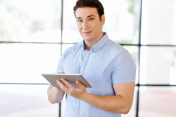 Młody przystojny biznesmen za pomocą jego stojące touchpad w biurze — Zdjęcie stockowe