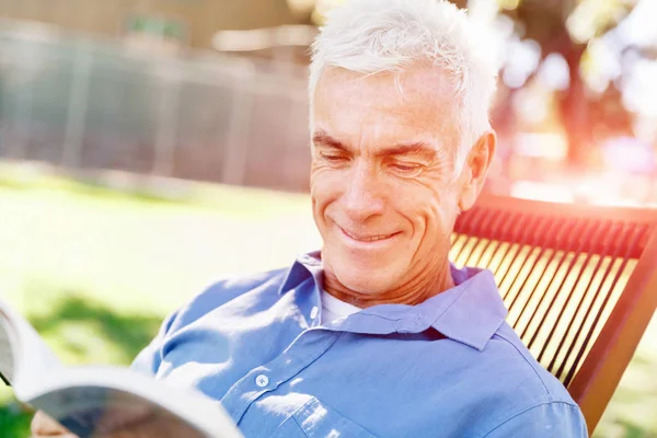 Senior man sittingin park tijdens het lezen van boek — Stockfoto