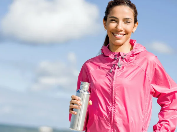 Schönes Mädchen in Sportkleidung trinkt Wasser nach dem Training am Strand — Stockfoto