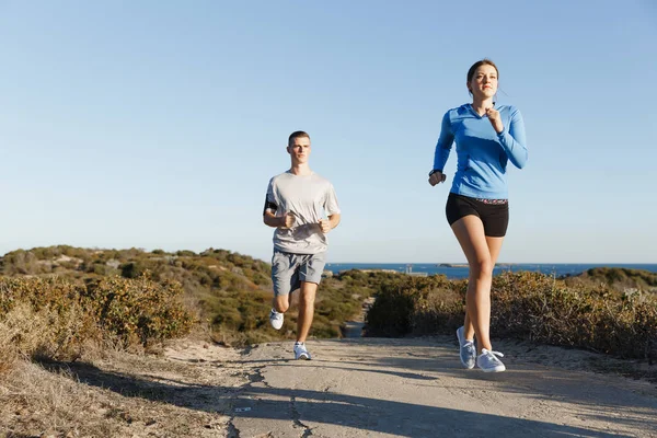 Sportlerin joggt mit ihrem Partner am Strand — Stockfoto