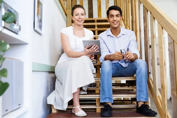Portrait of two young people sitting at the stairs in office — Stock Photo, Image