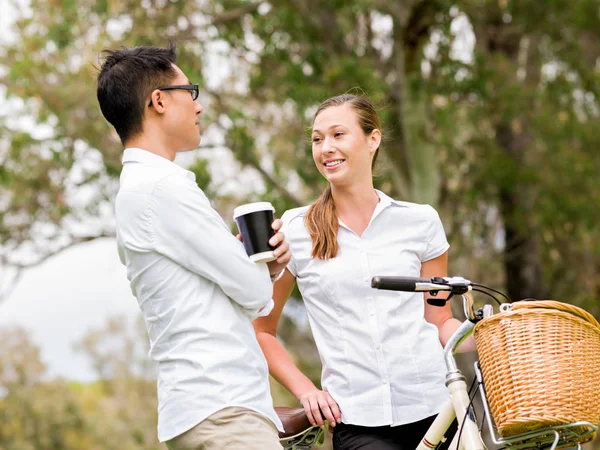 Portrait of smiling couple standing in park with bike talking — Stock Photo, Image