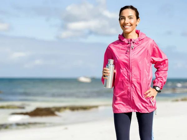 Belle fille en vêtements de sport boire de l'eau après l'entraînement sur la plage — Photo