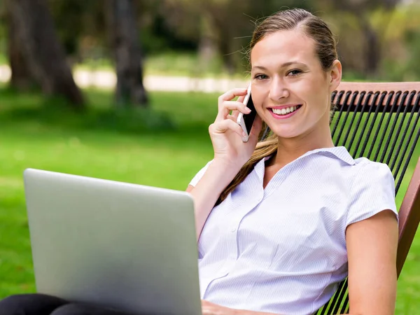 Mujer de negocios joven sentado en el parque y trabajando con el ordenador portátil —  Fotos de Stock