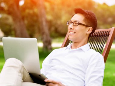 Genç işadamı açık havada otururken dizüstü bilgisayar kullanarak