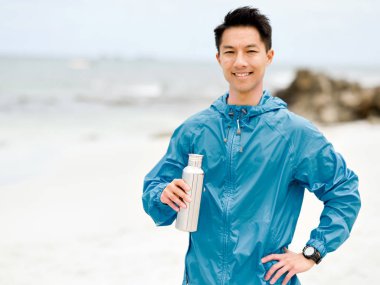 Sporda genç adam içme suyu egzersiz yaptıktan sonra kumsalda elbise