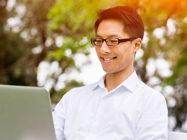 Genç işadamı açık havada otururken dizüstü bilgisayar kullanarak