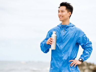 Sporda genç adam içme suyu egzersiz yaptıktan sonra kumsalda elbise