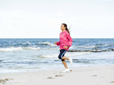 Genç bir kadın sahilde koşuyor.