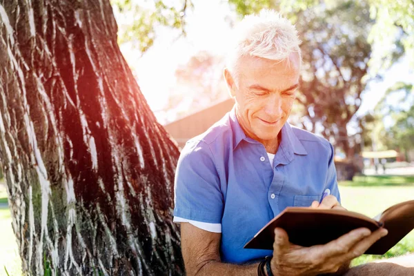 Senior homme assis dans le parc tout en lisant le livre — Photo