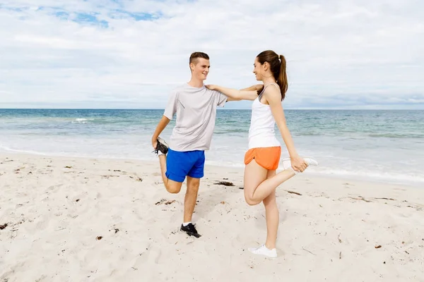 Corredores. Jovem casal exercitando e stertching na praia — Fotografia de Stock