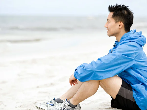 Молодой человек сидит на пляже в спортивной одежде — стоковое фото