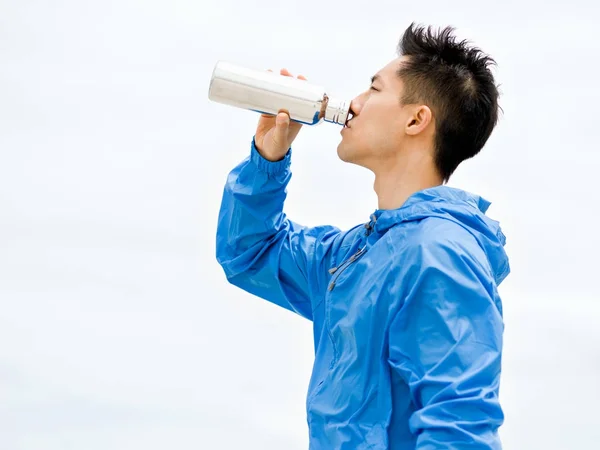 Junger Mann in Sportkleidung trinkt Wasser nach dem Training am Strand — Stockfoto