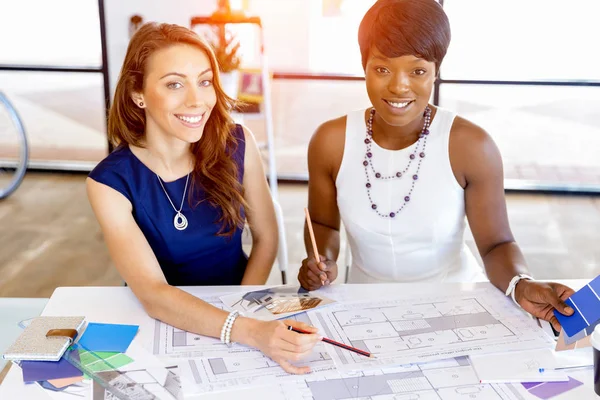 Jonge vrouwen zitten aan een bureau in een kantoor en werken op de blauwdruk — Stockfoto